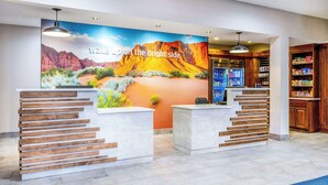 A reception area with a desert-themed mural, wooden reception desks, and a beverage refrigerator. - La Quinta Inn & Suites by Wyndham St. George (St. George)