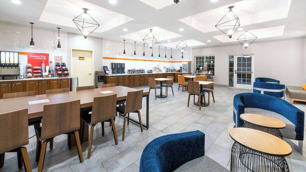 A modern dining area with wooden tables and chairs, a coffee station, and a seating area with blue sofas and round tables. - La Quinta Inn & Suites by Wyndham St. George (St. George)