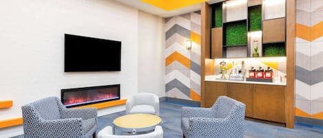 A modern lounge area with a flat-screen TV, a fireplace, and a bar counter with various amenities.