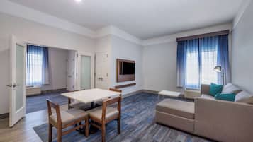 A modern living room with a dining area, a sofa, a TV mounted on the wall, and a window with curtains.