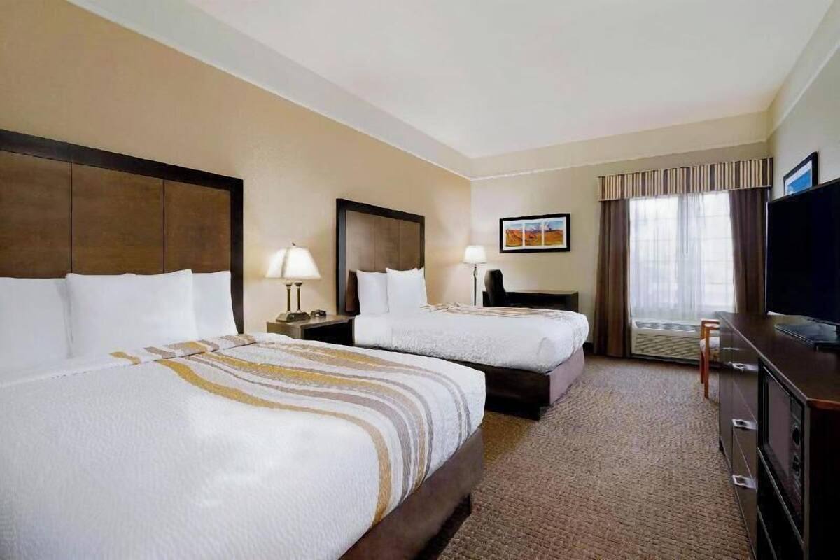 A hotel room with two beds, a television, a desk, and a large window with curtains.