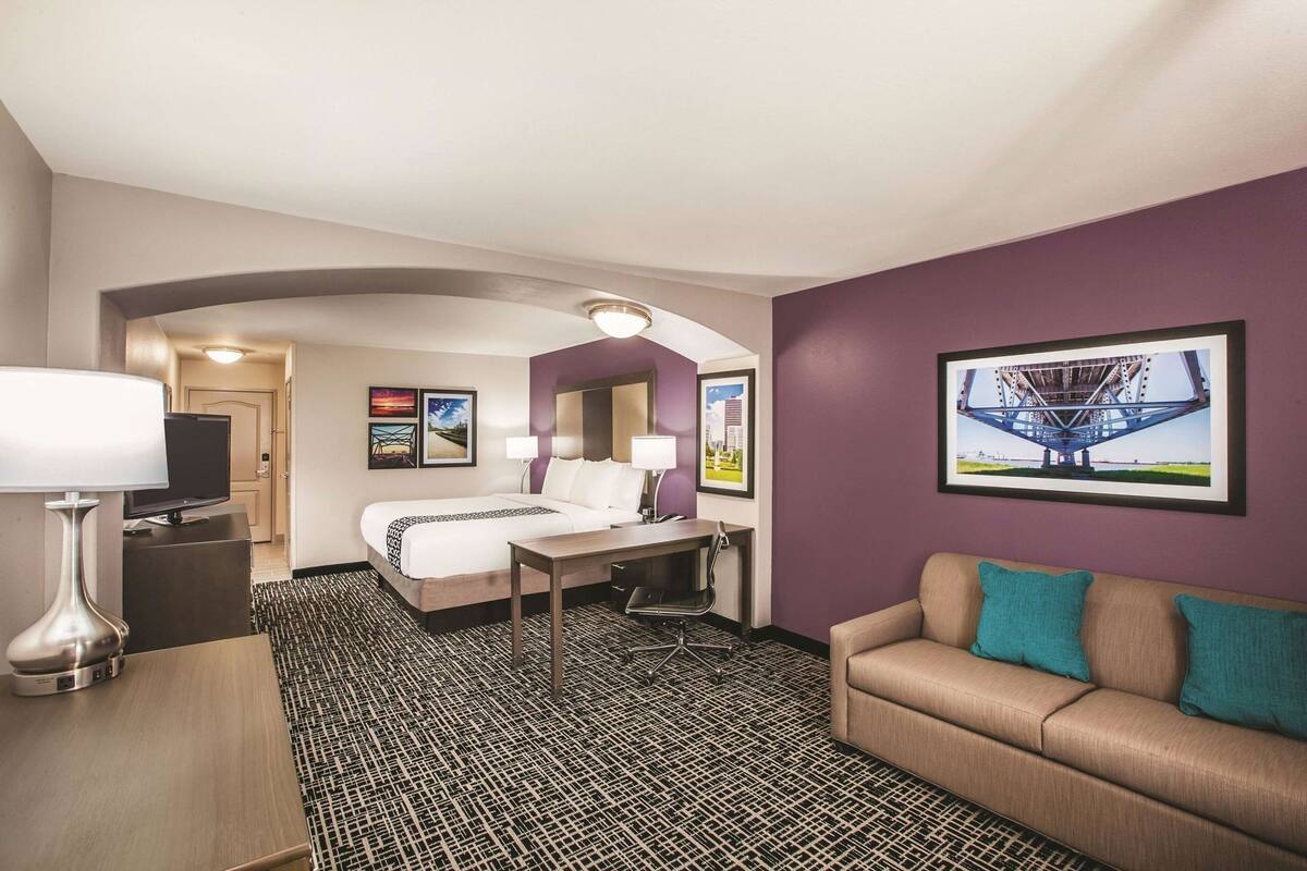 Habitación de hotel con cama, escritorio, sofá, televisión y cuadros en las paredes.