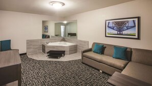 Une chambre d’hôtel moderne avec une grande baignoire, un canapé agrémenté de coussins turquoise et un tableau représentant un pont, accroché au mur.