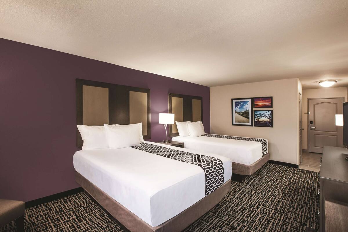 Habitación de hotel con dos camas, alfombra estampada y una puerta a la derecha.