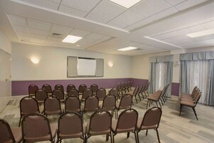 Un salón de conferencias con filas de sillas, una pantalla de proyector y una pizarra.