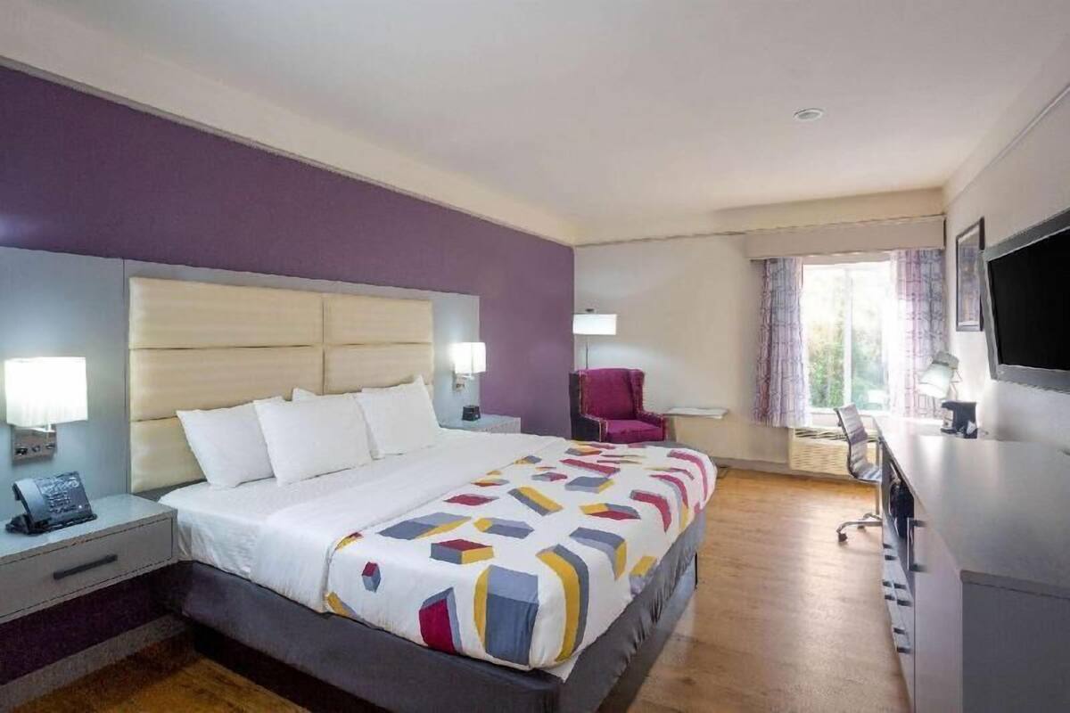 A hotel room with a bed, bedside table, lamp, chair, desk, and TV.