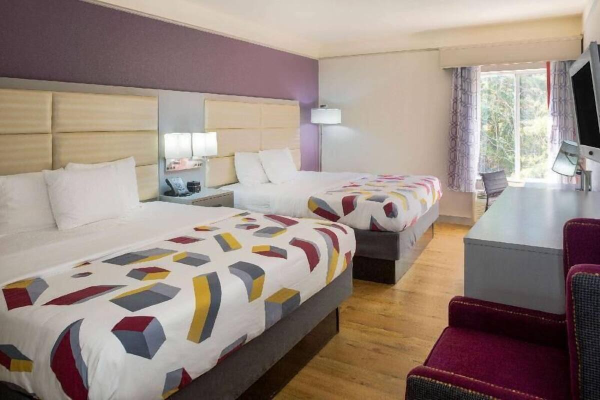 A hotel room with two beds, a desk, a chair, and a TV.
