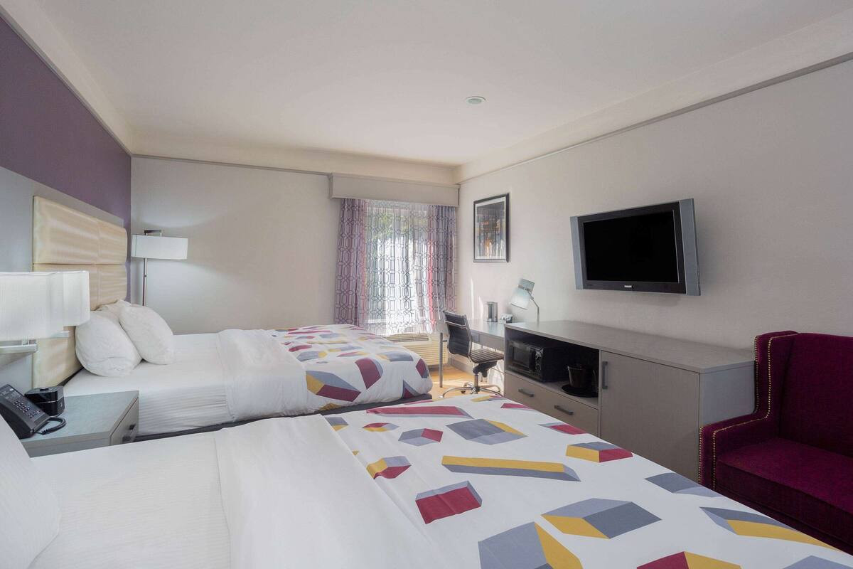 A hotel room with two beds, a desk, a chair, a TV, and a phone on the nightstand.