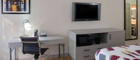A hotel room with a desk, chair, bed, TV, and a mirror.