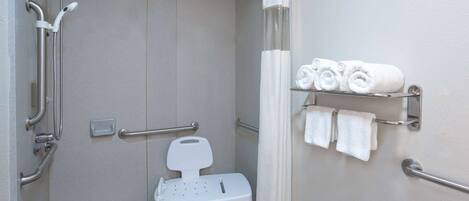 A bathroom with a shower, grab bars, a white toilet, and a towel rack with towels.