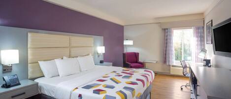 A hotel room with a bed, bedside table, lamp, chair, desk, and TV.
