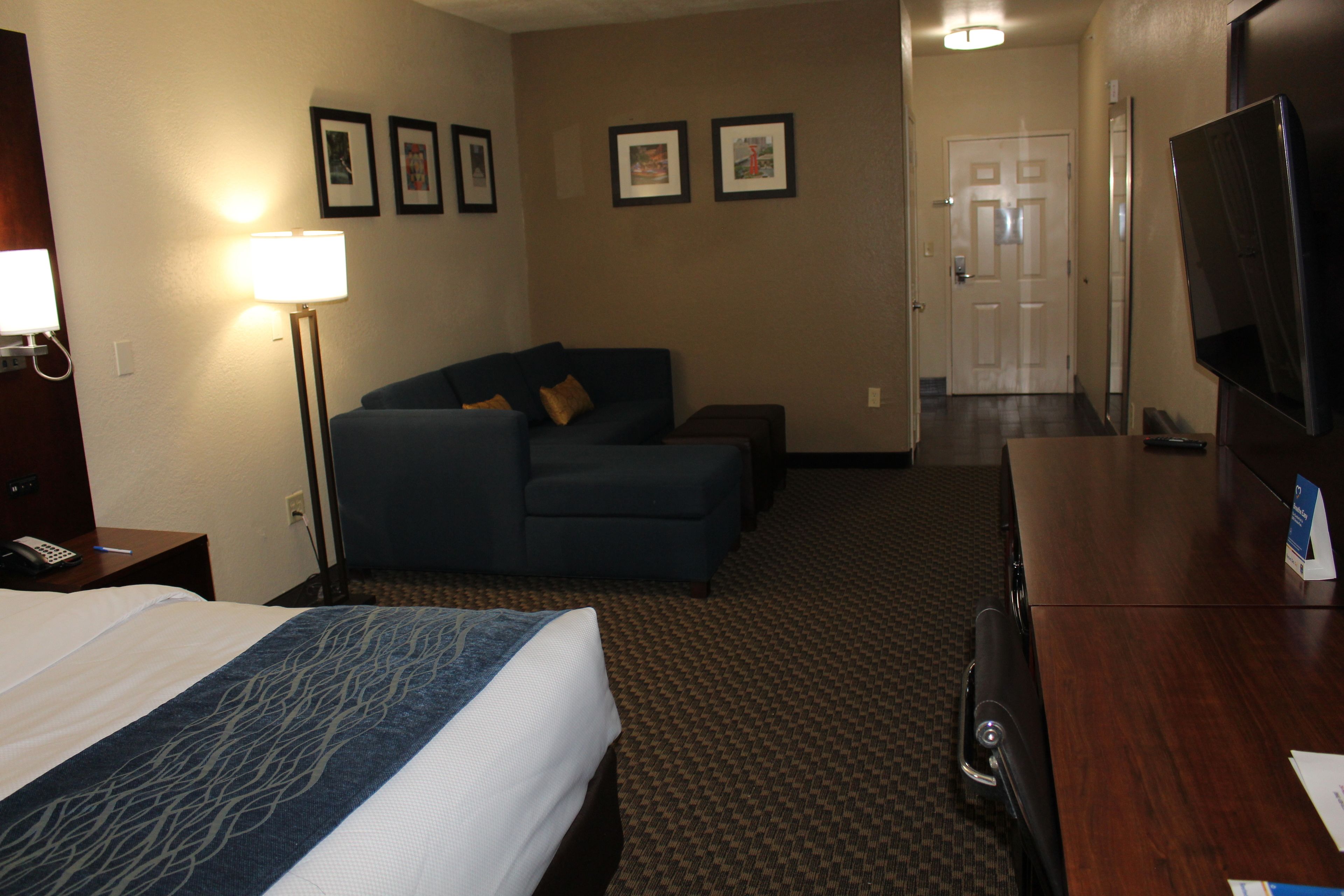 A hotel room with a bed, a sofa, a desk, a TV, and framed pictures on the wall.