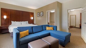 Une chambre d’hôtel avec un grand lit, un canapé bleu avec un pouf marron et une tête de lit en bois.