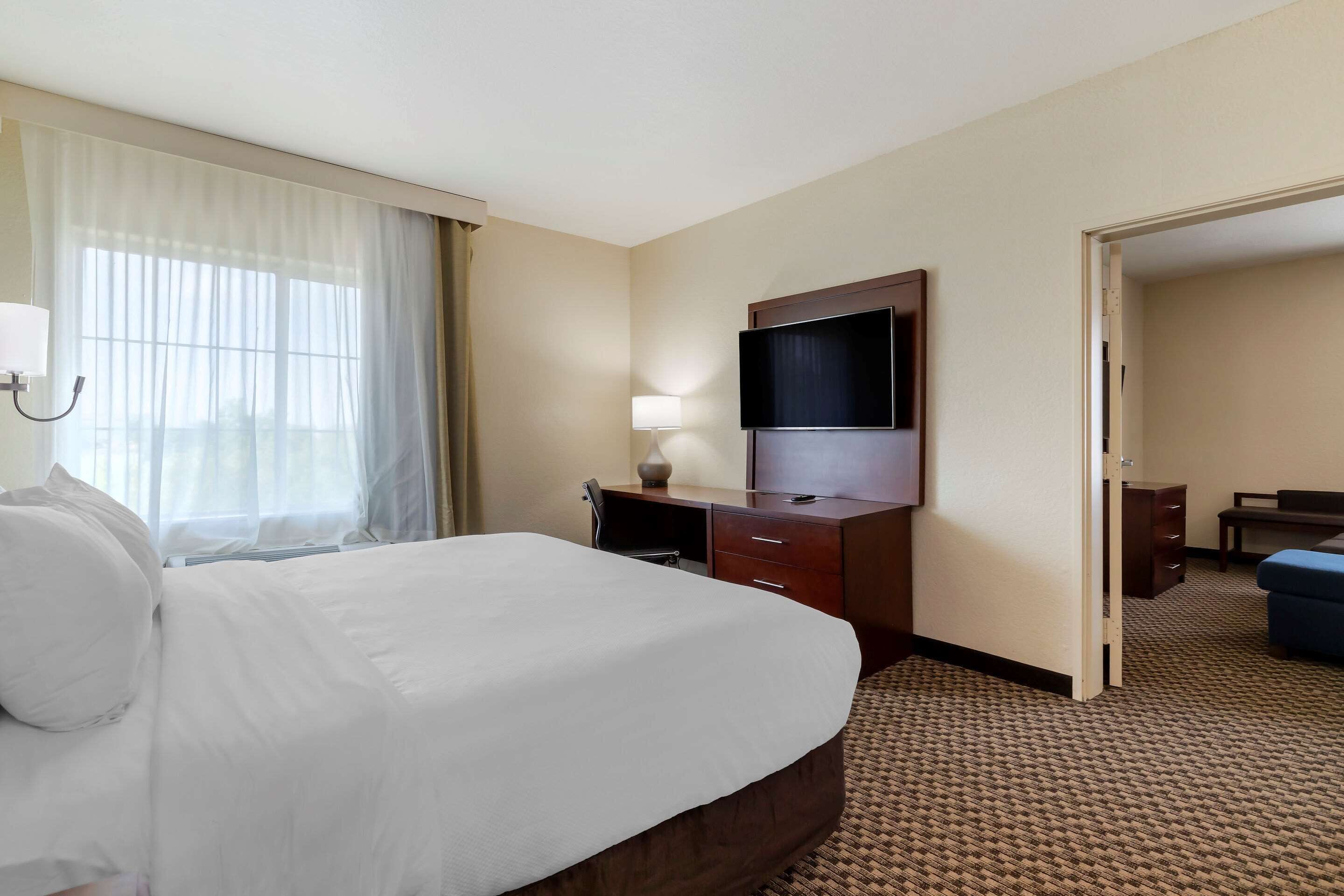 Una habitación de hotel con una cama grande, un escritorio, un televisor y una puerta que da a otra habitación.