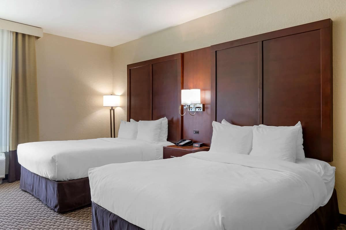 Une chambre d’hôtel avec deux lits, une table de chevet avec une lampe et un téléphone fixé au mur.