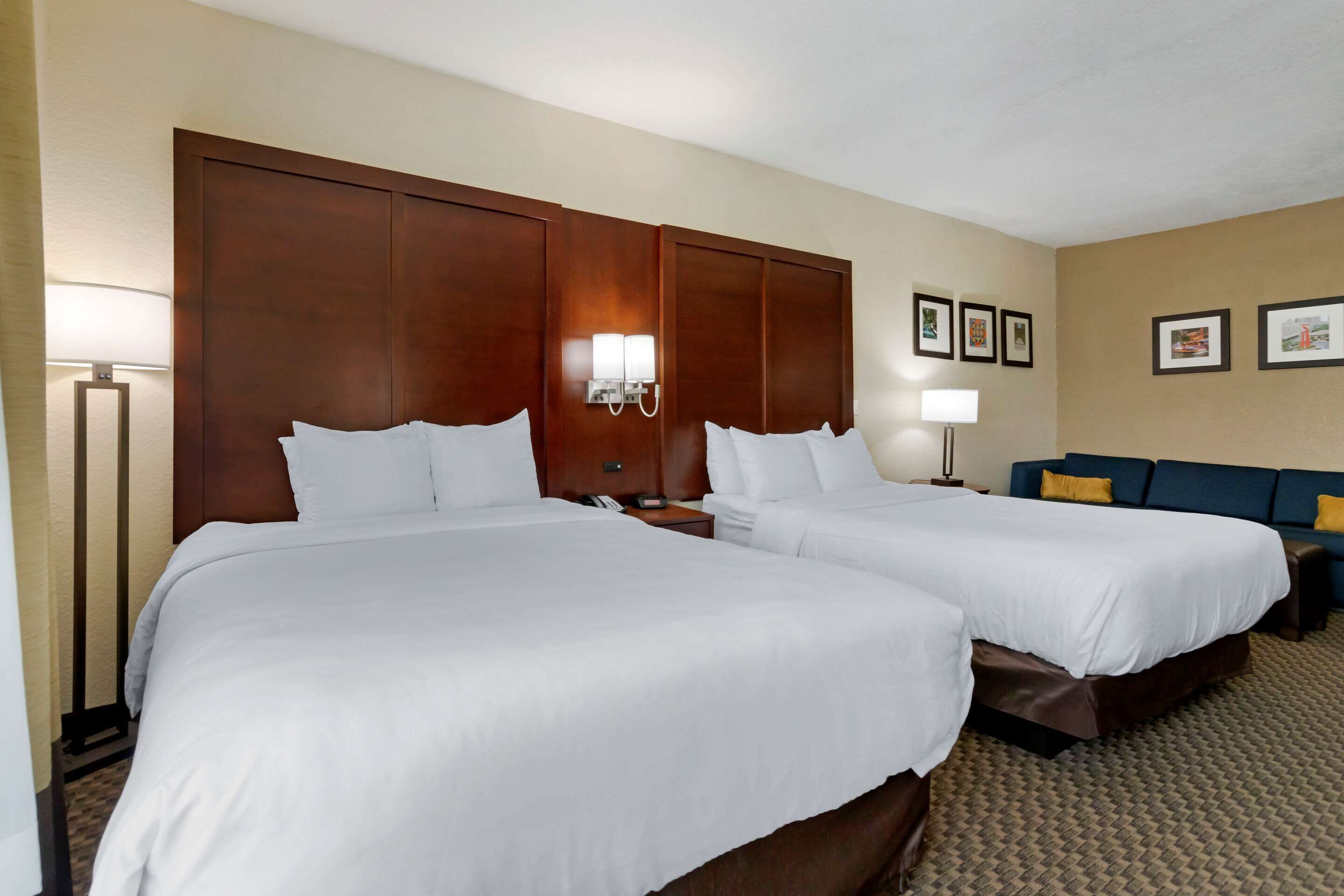A hotel room with two single beds, a sofa, a lamp, and framed pictures on the wall.