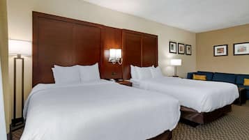 A hotel room with two single beds, a sofa, a lamp, and framed pictures on the wall.