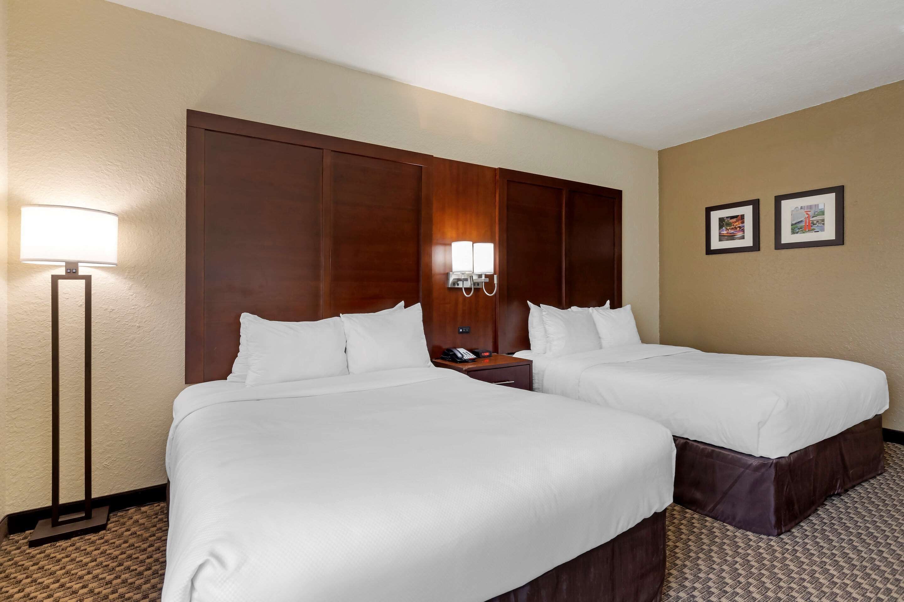 A hotel room with two single beds, a nightstand with a phone, a lamp, and two framed pictures on the wall.
