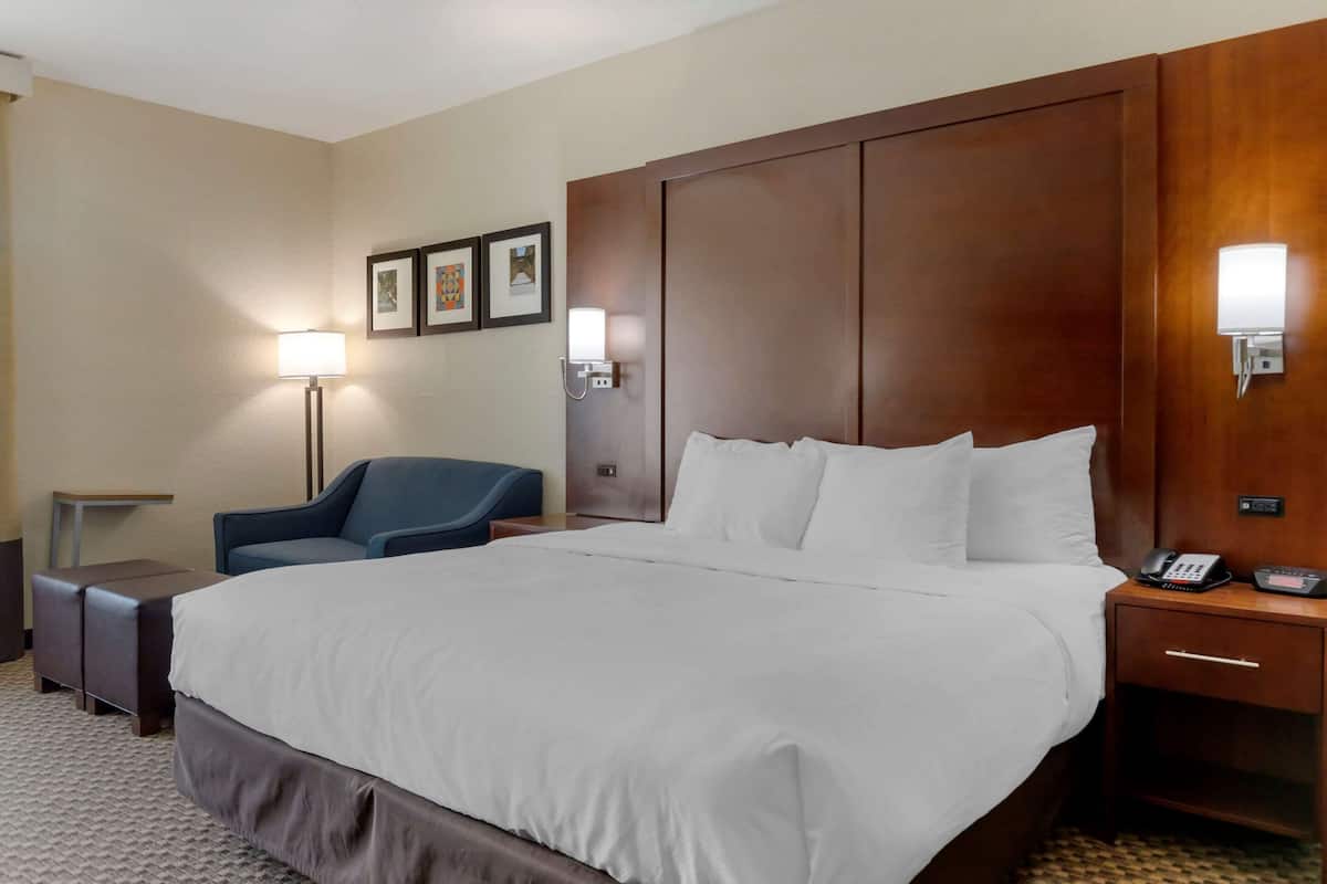 Une chambre d’hôtel avec un grand lit, un bureau, une chaise, une table de chevet avec un téléphone et des lampes fixées au mur.