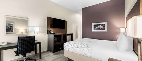 A hotel room with a bed, desk, chair, TV, and a small table.
