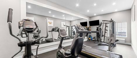 Un gimnasio con equipamiento de ejercicio, un espejo grande y una ventana.