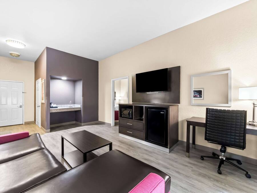 Una habitación de hotel moderna con zona de estar, kitchenette, televisor de pantalla plana, escritorio y un espacio de descanso confortable.