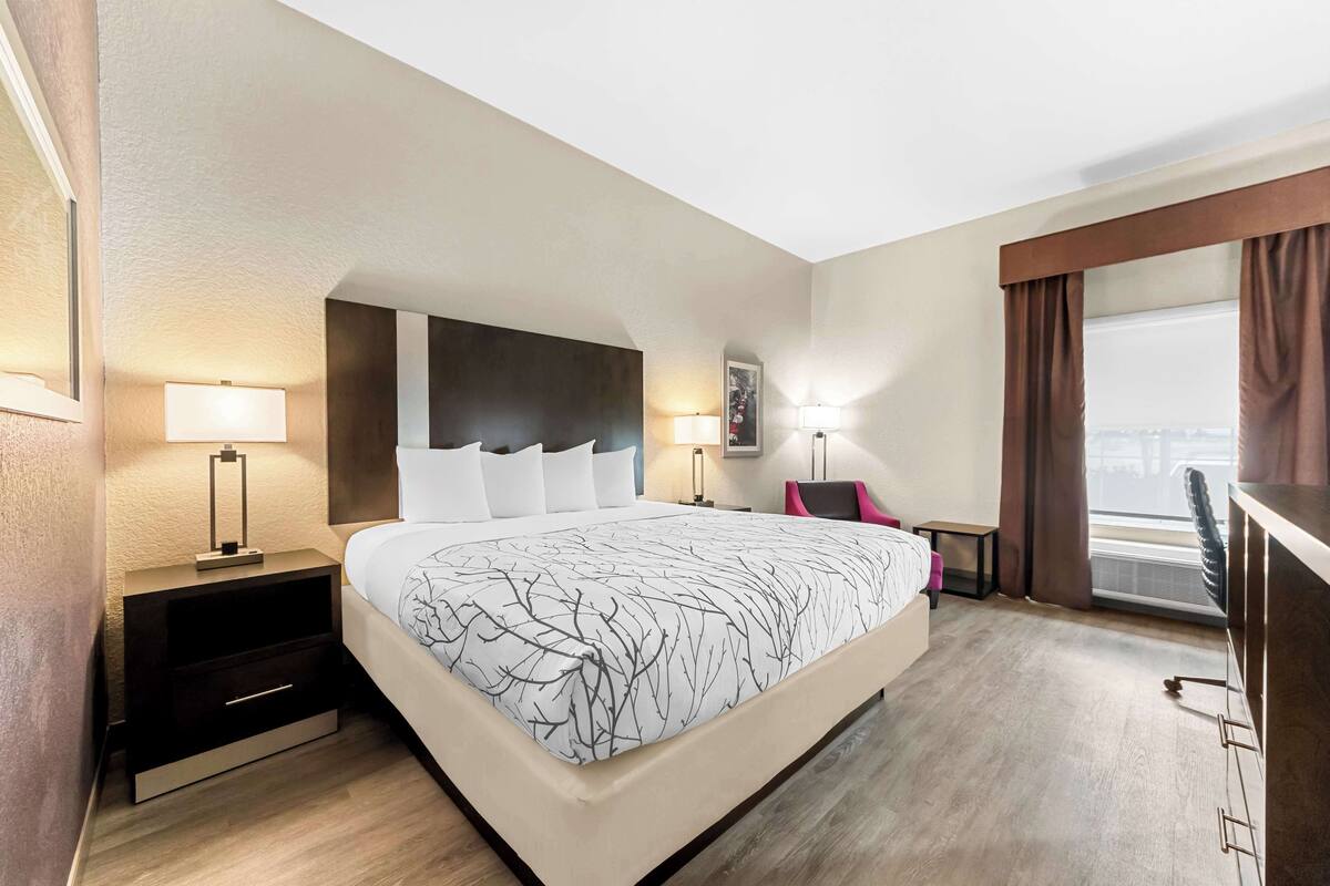 Une chambre d’hôtel avec un grand lit, des tables de chevet avec des lampes, un bureau et une vue sur la ville par la fenêtre.