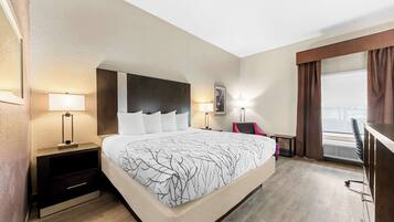 Quarto de hotel com uma cama grande, mesas de cabeceira com abajures, uma escrivaninha e vista para a cidade pela janela.