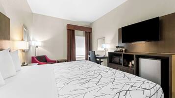 A hotel room with a large bed, a desk with a flat-screen TV, a microwave, and a refrigerator.