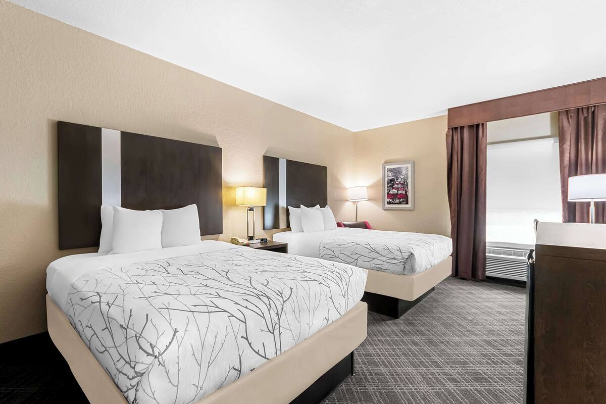 Une chambre d’hôtel avec deux lits, un bureau, une lampe et une fenêtre avec des rideaux.