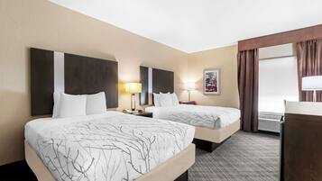 A hotel room with two beds, a desk, a lamp, and a window with curtains.