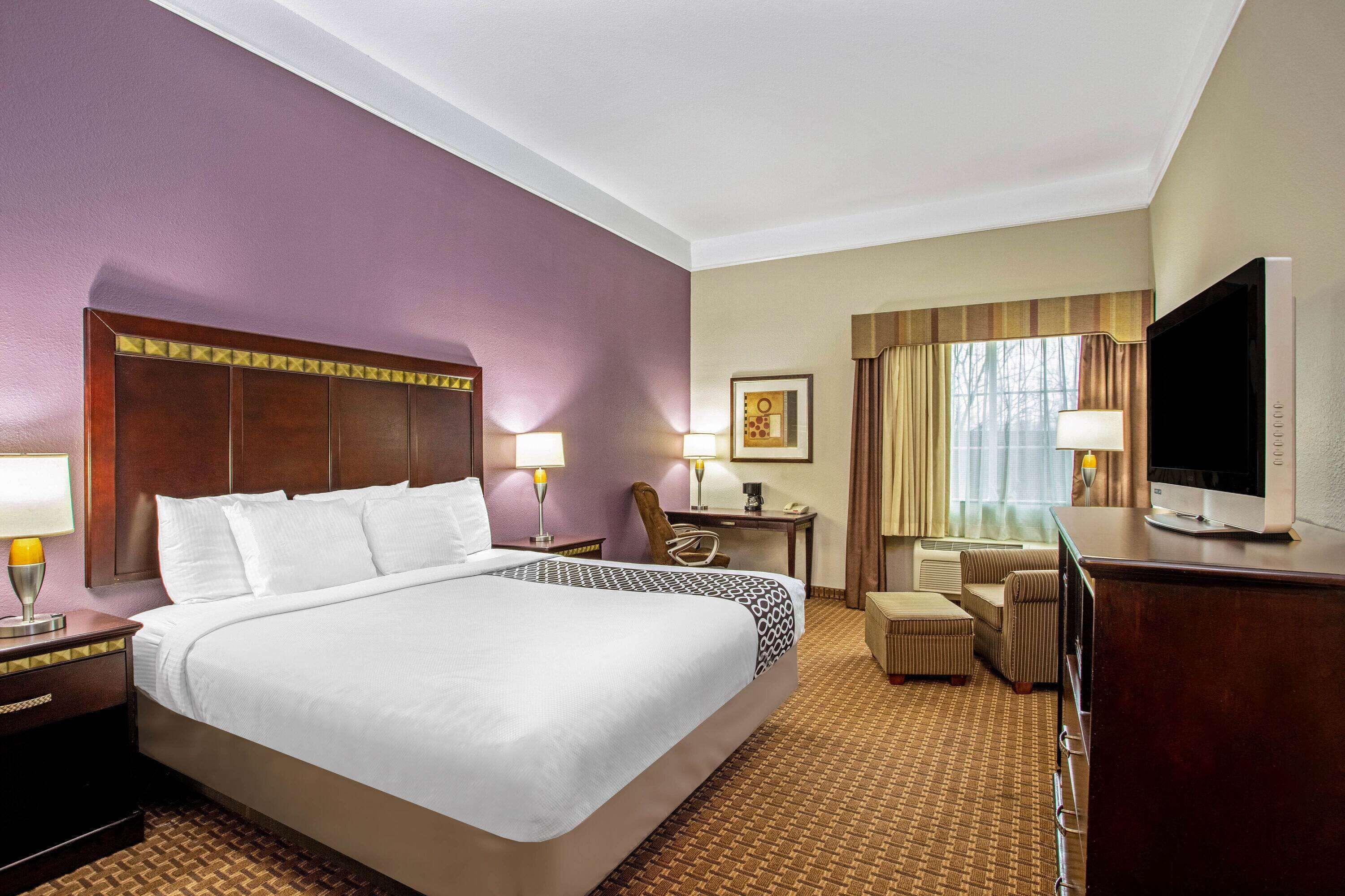 Habitación de hotel con una cama grande, un escritorio con silla, televisor y ventana con cortinas.