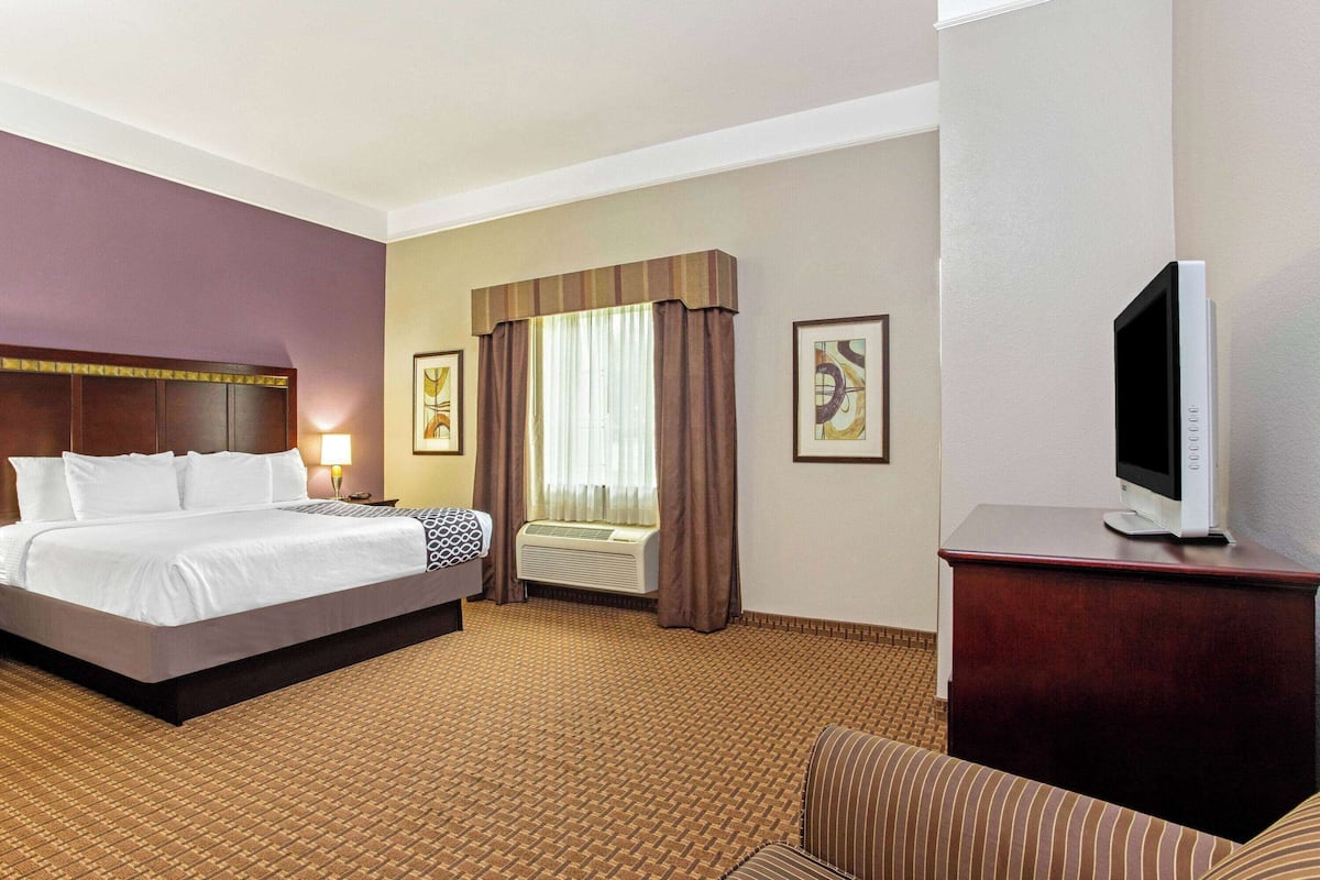 A hotel room with a large bed, a TV on a wooden cabinet, a window with curtains, and a carpeted floor.