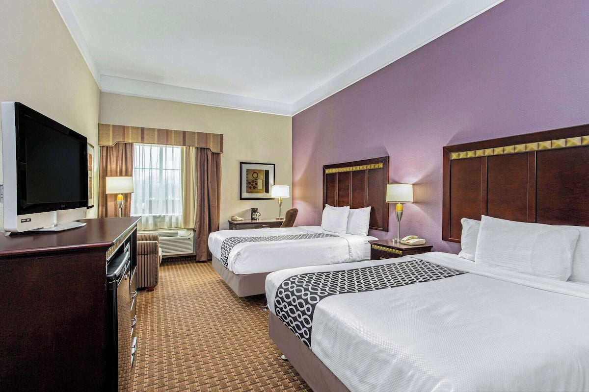 A hotel room with two beds, a TV, a desk, and a chair.