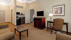 Une chambre d’hôtel équipée d’une kitchenette, d’un téléviseur à écran plat, d’un bureau avec une lampe, d’un fauteuil en cuir marron et d’un canapé à rayures.