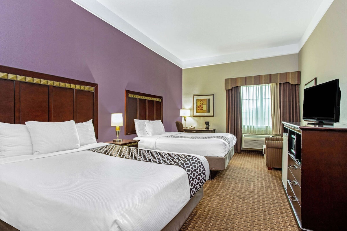 A hotel room with two beds, a television, a desk, and a window with curtains.