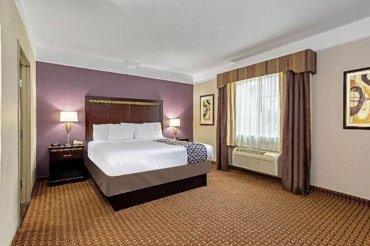 A hotel room with a bed, two bedside tables, a window with curtains, and a wall-mounted air conditioning unit.