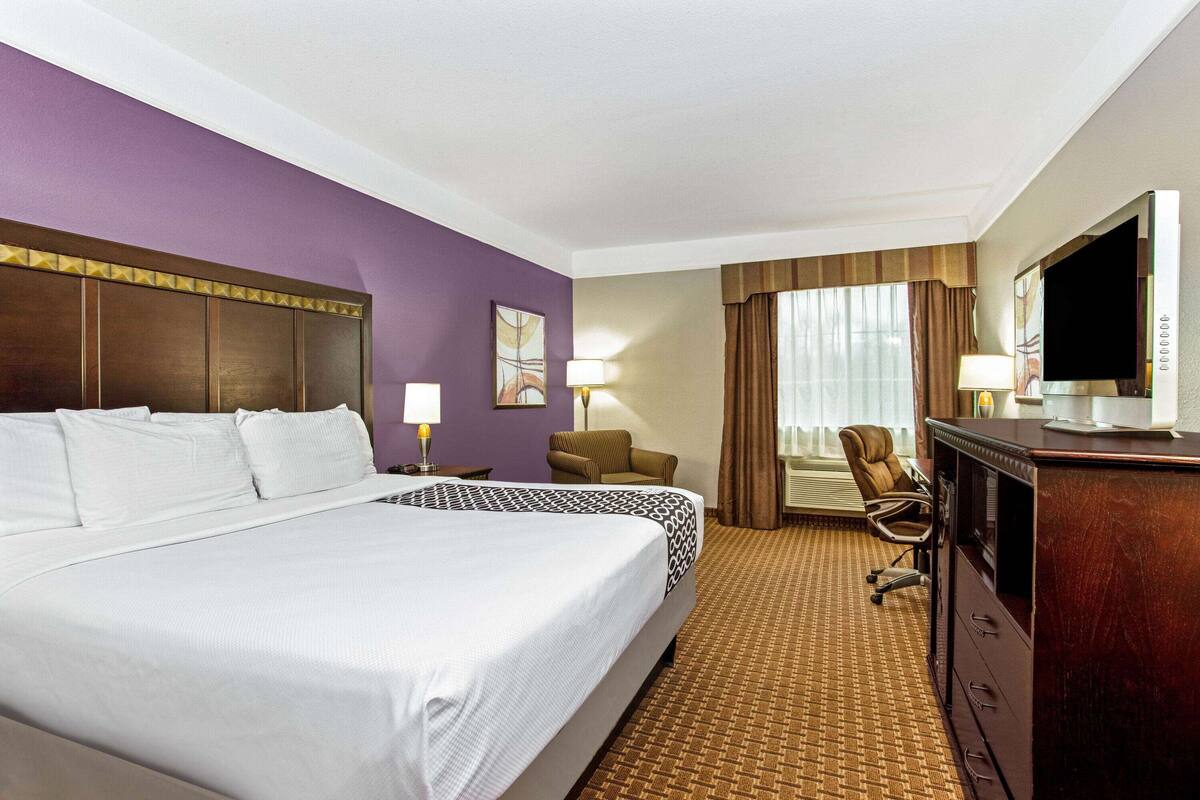 A hotel room with a large bed, a desk with a TV, a chair, and a lamp.