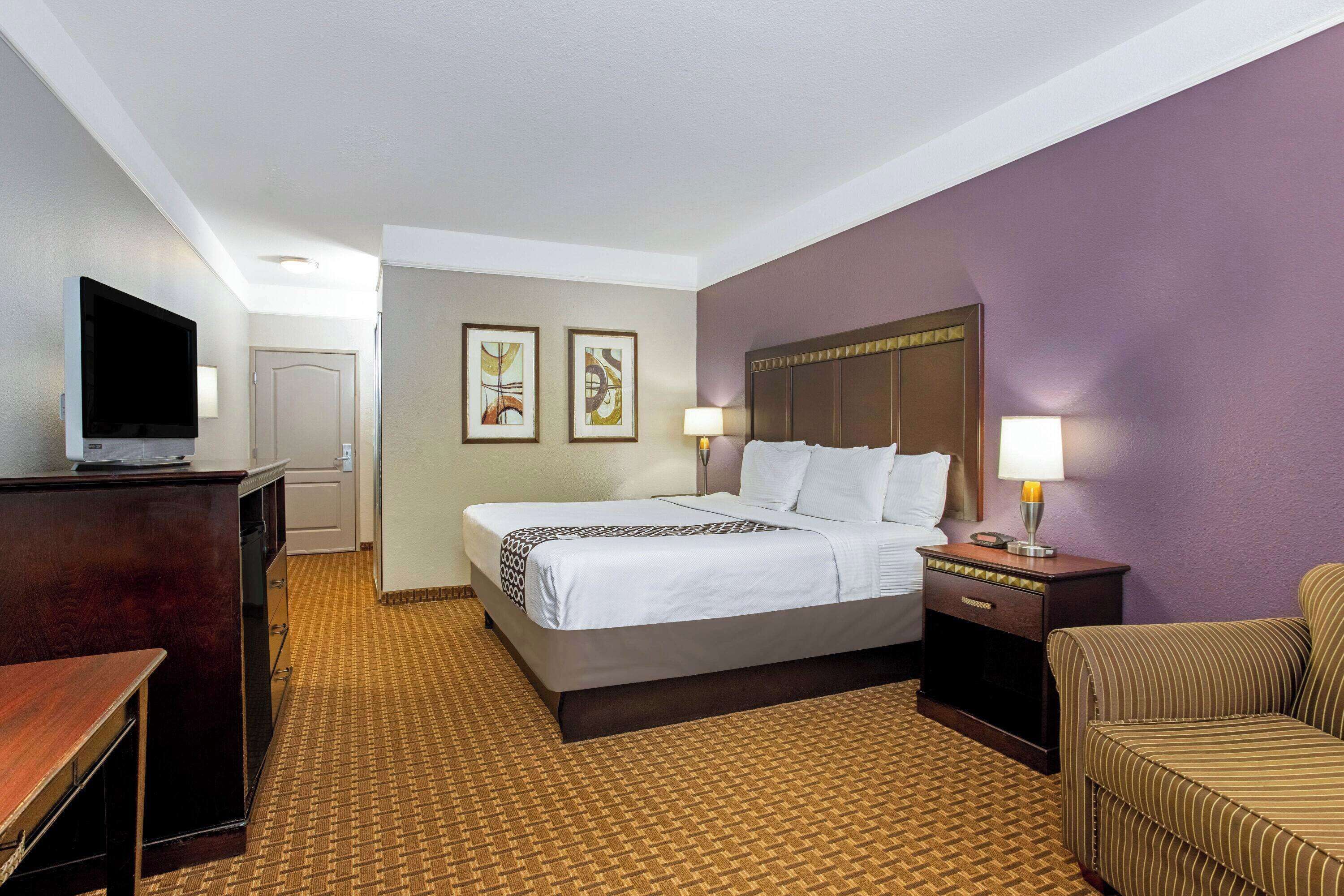 A hotel room with a bed, a desk, a TV, and two wall-mounted paintings.