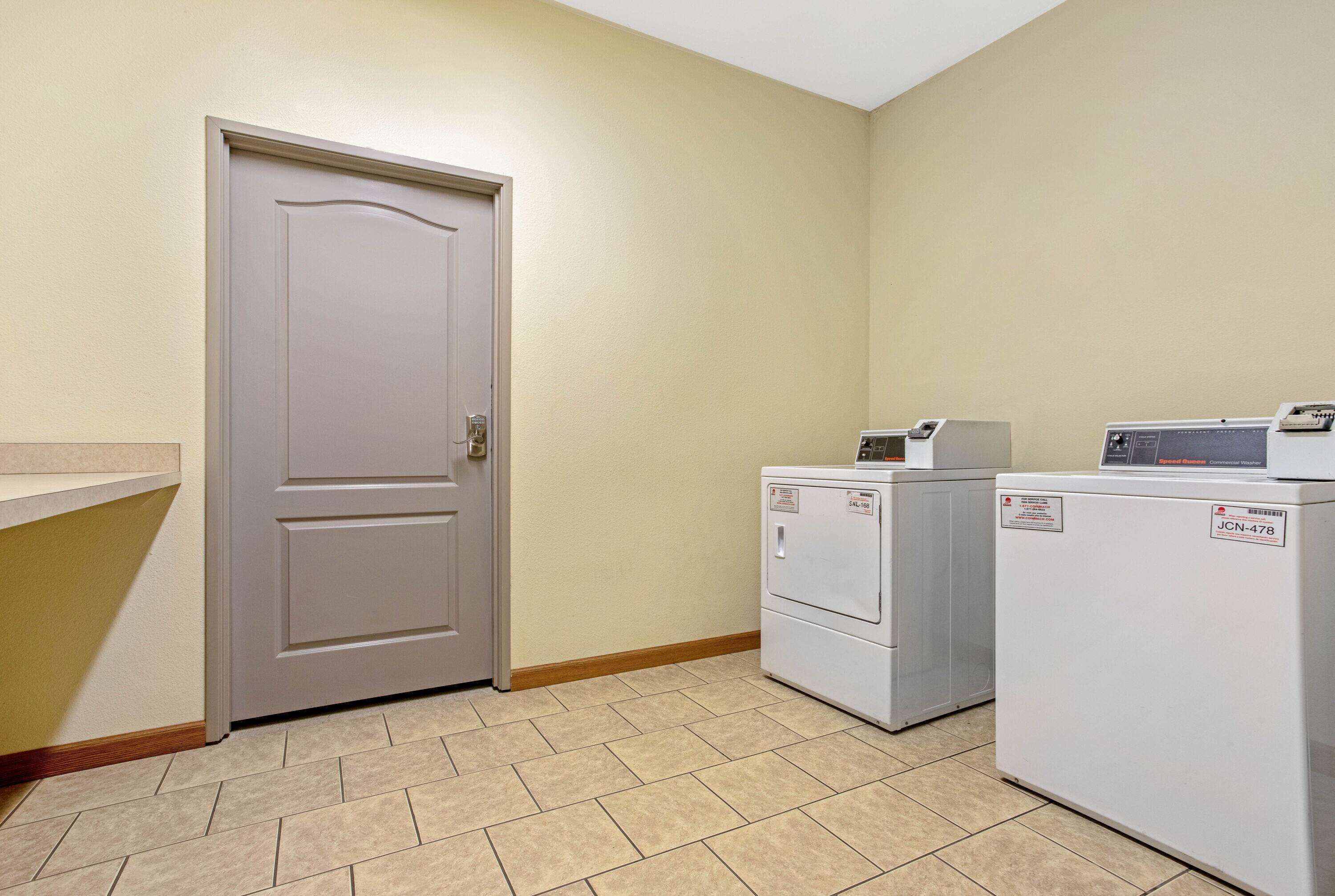 A laundry room with two stacked washers and a dryer, a beige door, and a tiled floor.