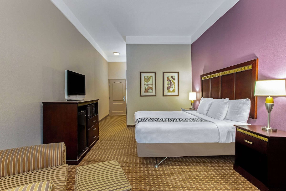 A hotel room with a bed, a television on a dresser, a desk with a lamp, and two framed pictures on the wall.