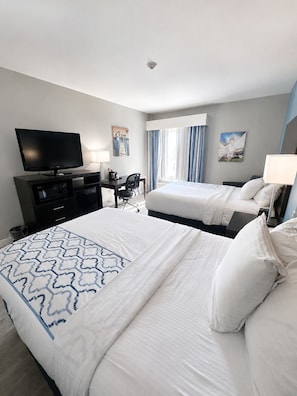 A hotel room with two beds, a desk, a television, and a window with curtains.