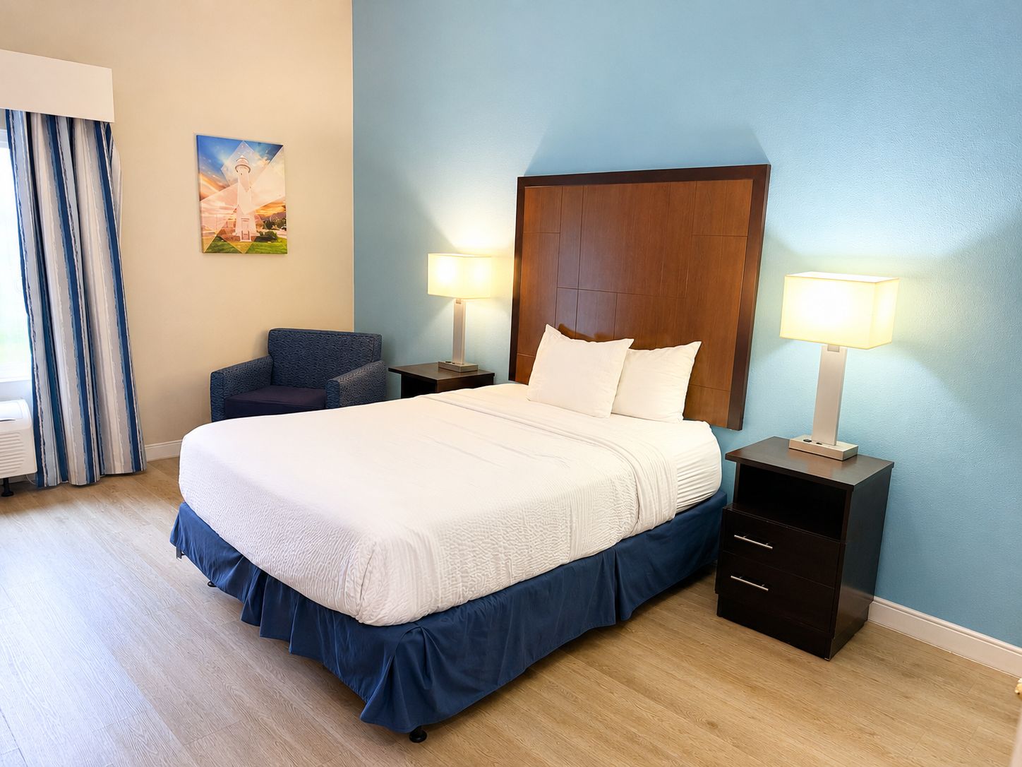 Ein Hotelzimmer mit einem großen Bett, zwei Nachttischen, einem Sessel und einem Gemälde an der Wand.