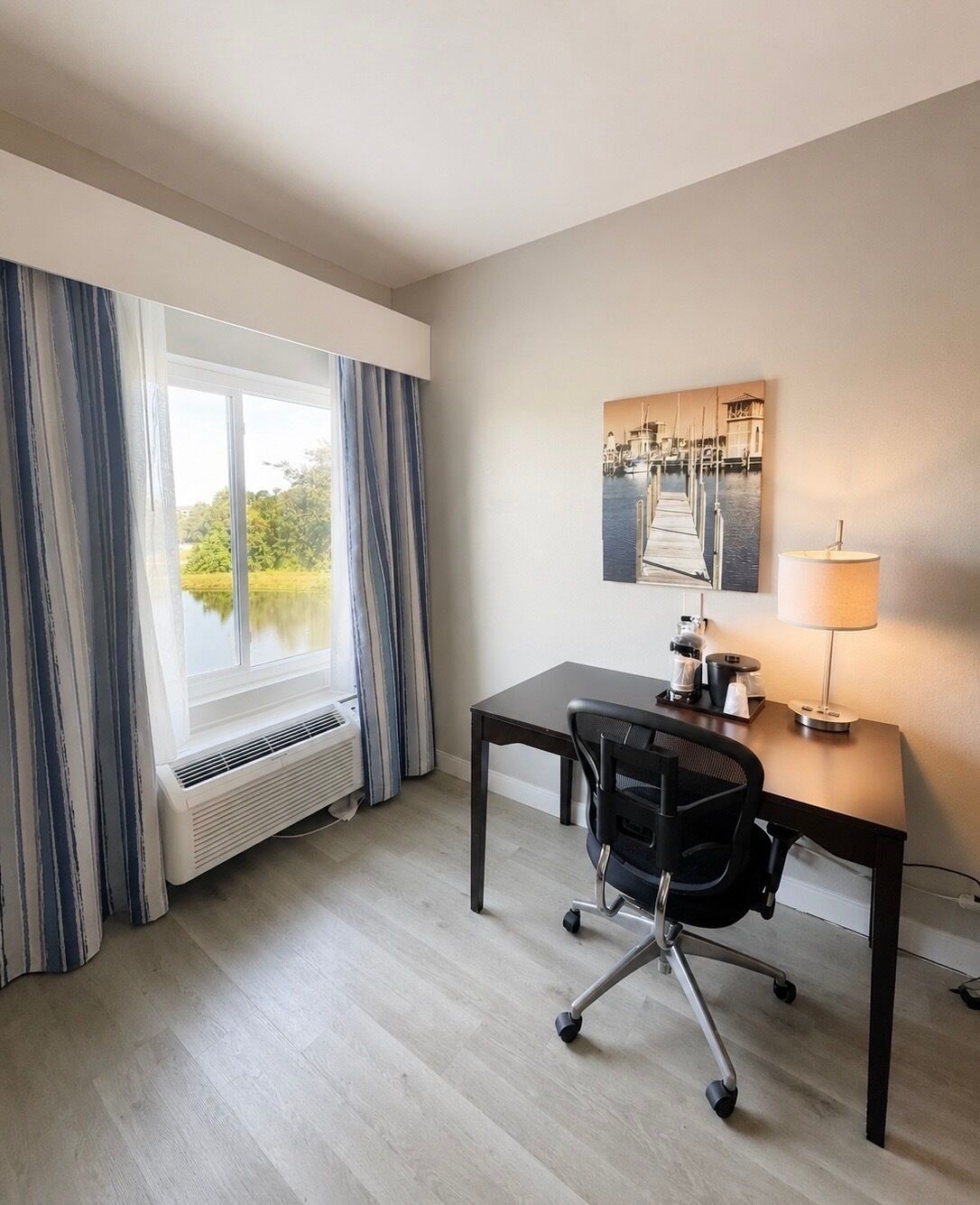 A hotel room with a desk, chair, lamp, and a window with curtains.