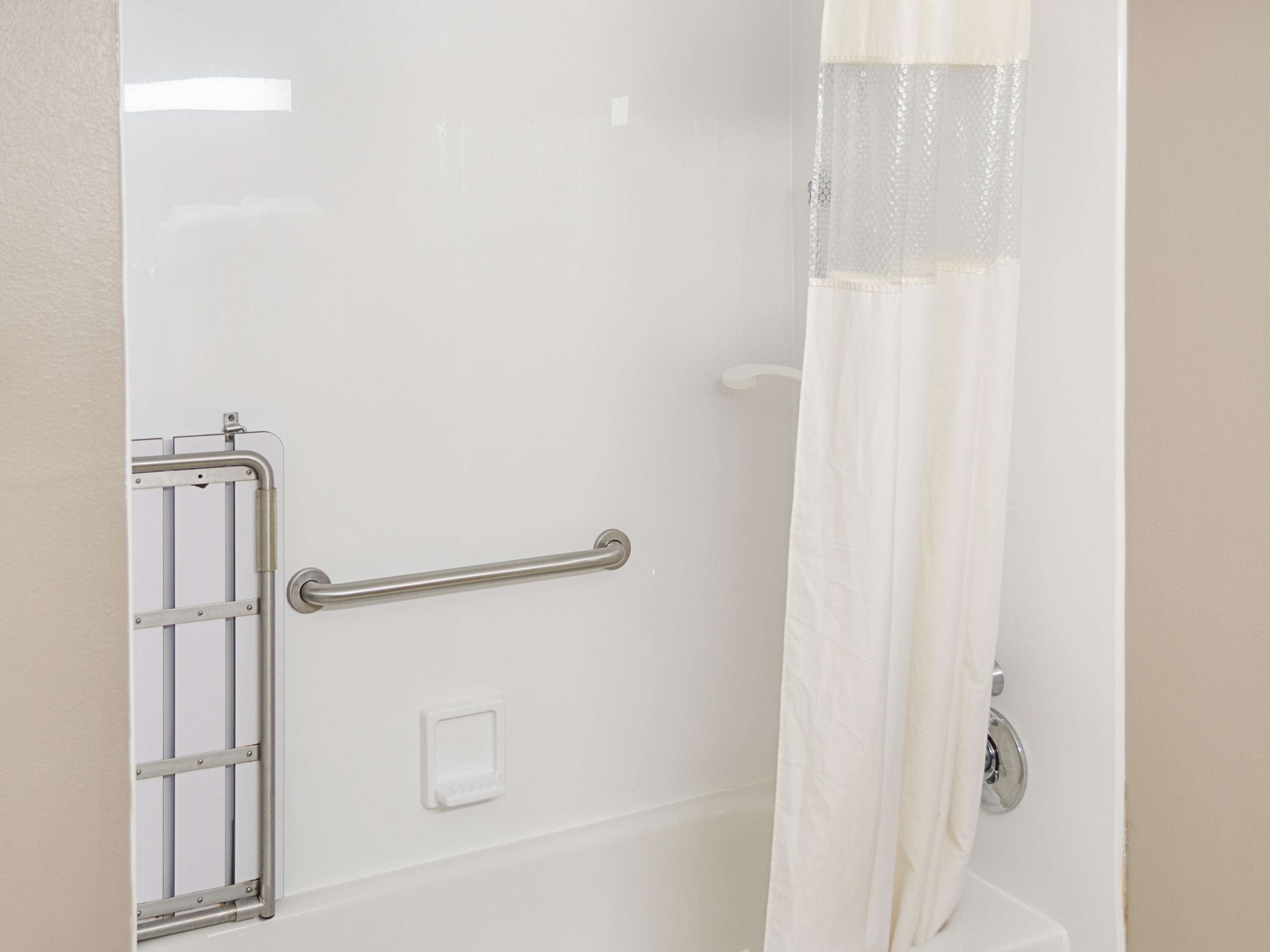 A shower area with a grab bar, a white wall, and a shower curtain.