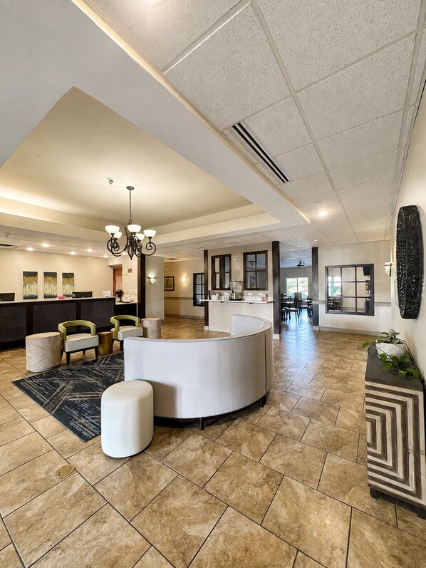A spacious lobby with a reception desk, seating area, and a kitchen in the background.