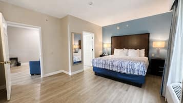 A hotel room with a large bed, bedside lamps, a door leading to another room, and a visible air conditioning unit.