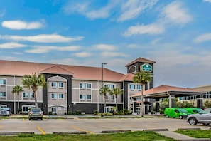 Um hotel com uma placa visível, vários espaços de estacionamento e uma área ajardinada bem cuidada.