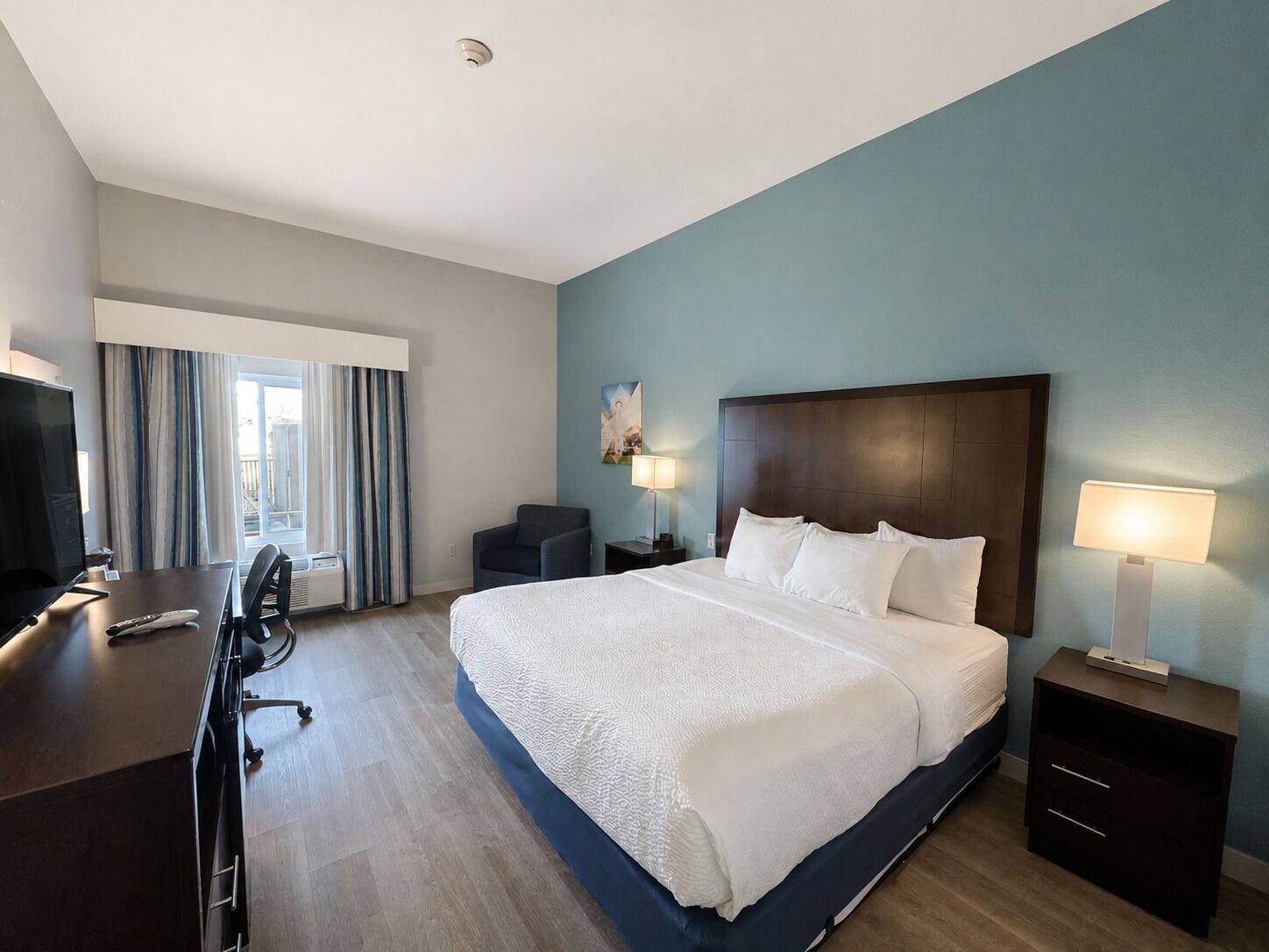 Una habitación de hotel con una cama grande, un escritorio con silla, un televisor y una ventana con cortinas.