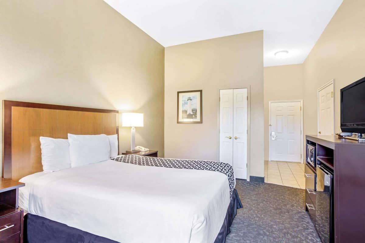 Une chambre d’hôtel comprenant un lit, une lampe de chevet, un bureau, une télévision, une armoire et un tableau encadré au mur.